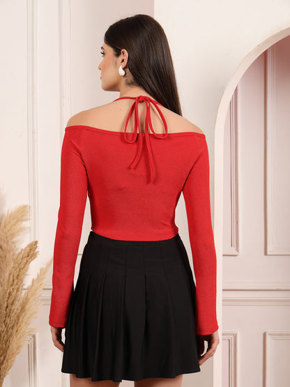 Woman wearing a red off-shoulder top and black skirt against a white wall.