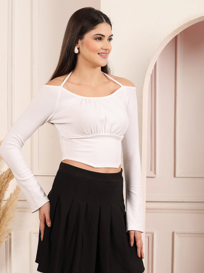 Woman wearing a white long-sleeve top and black skirt standing against a light-colored wall.