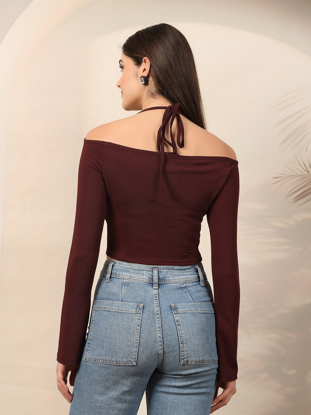 Woman wearing a burgundy off-shoulder top and blue jeans against a beige background
