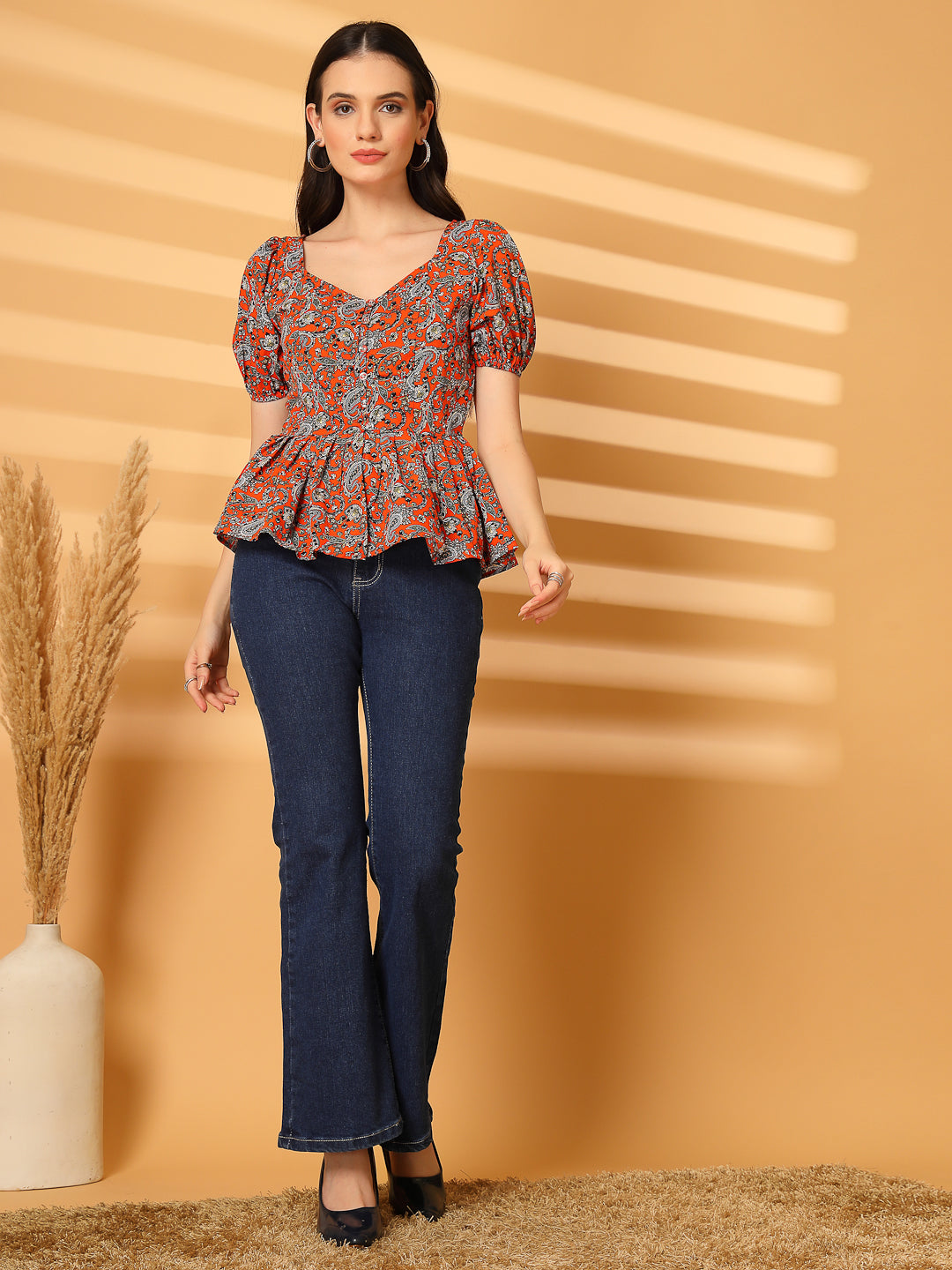 Woman wearing a patterned top and jeans against a beige background