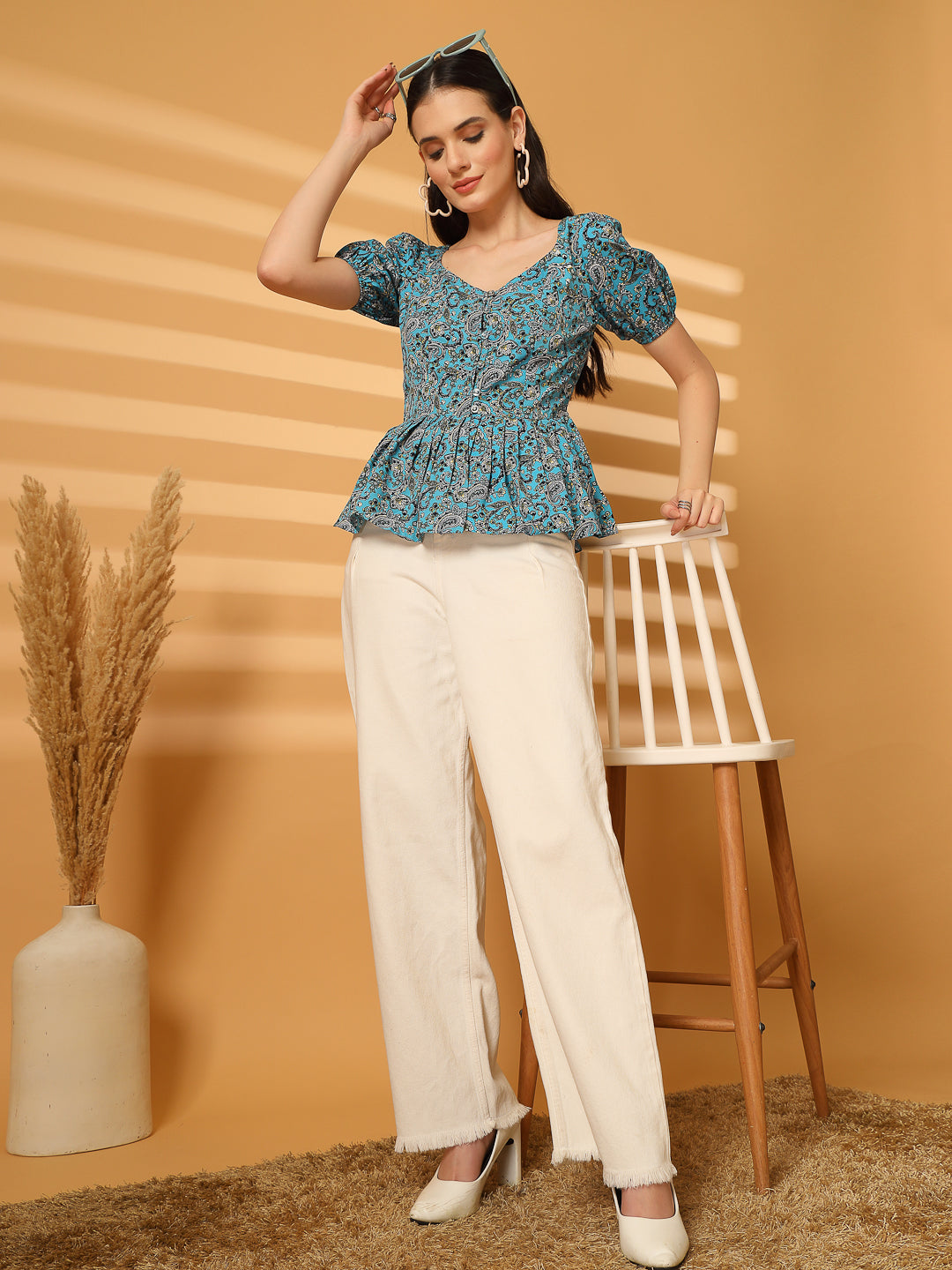 Woman wearing a blue floral top and white pants against a beige background