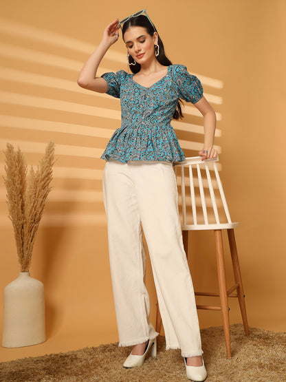 Woman wearing a blue floral top and white pants against a beige background