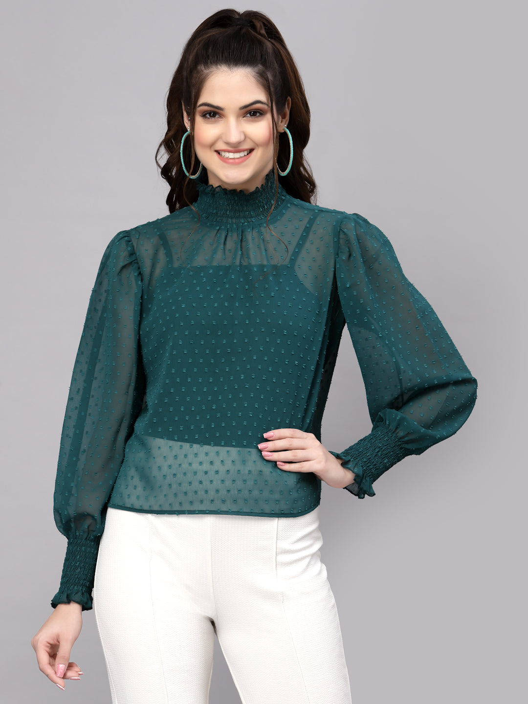 Woman wearing a green blouse with sheer sleeves on a gray background