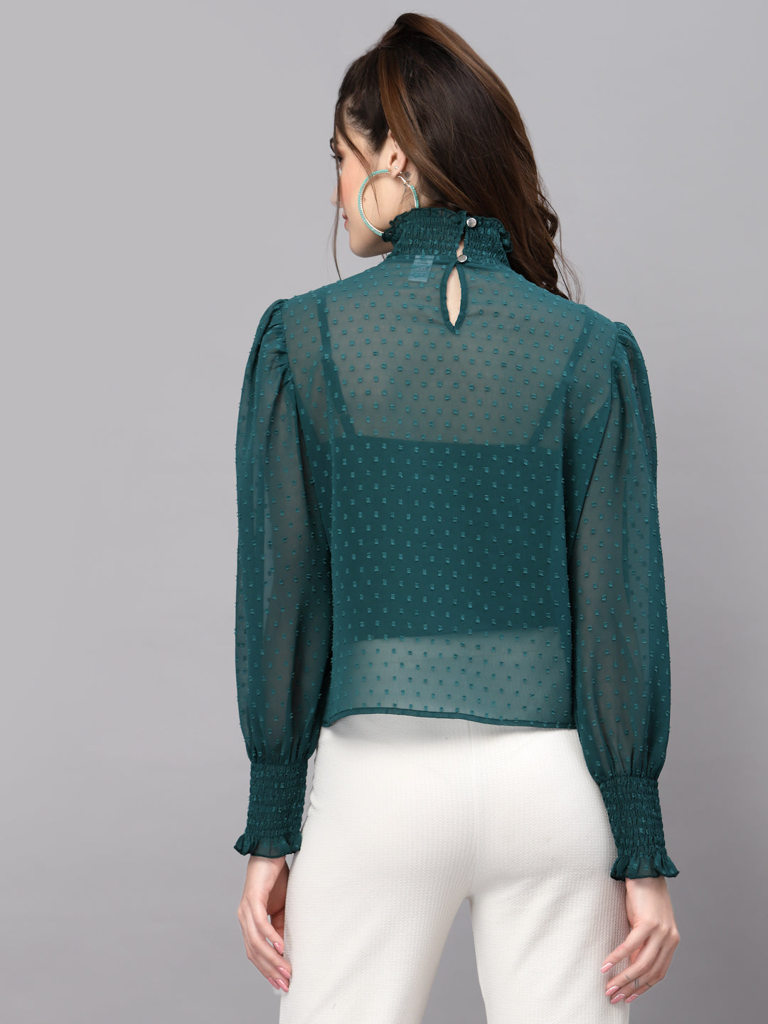 Woman wearing a green sheer blouse with white pants on a gray background
