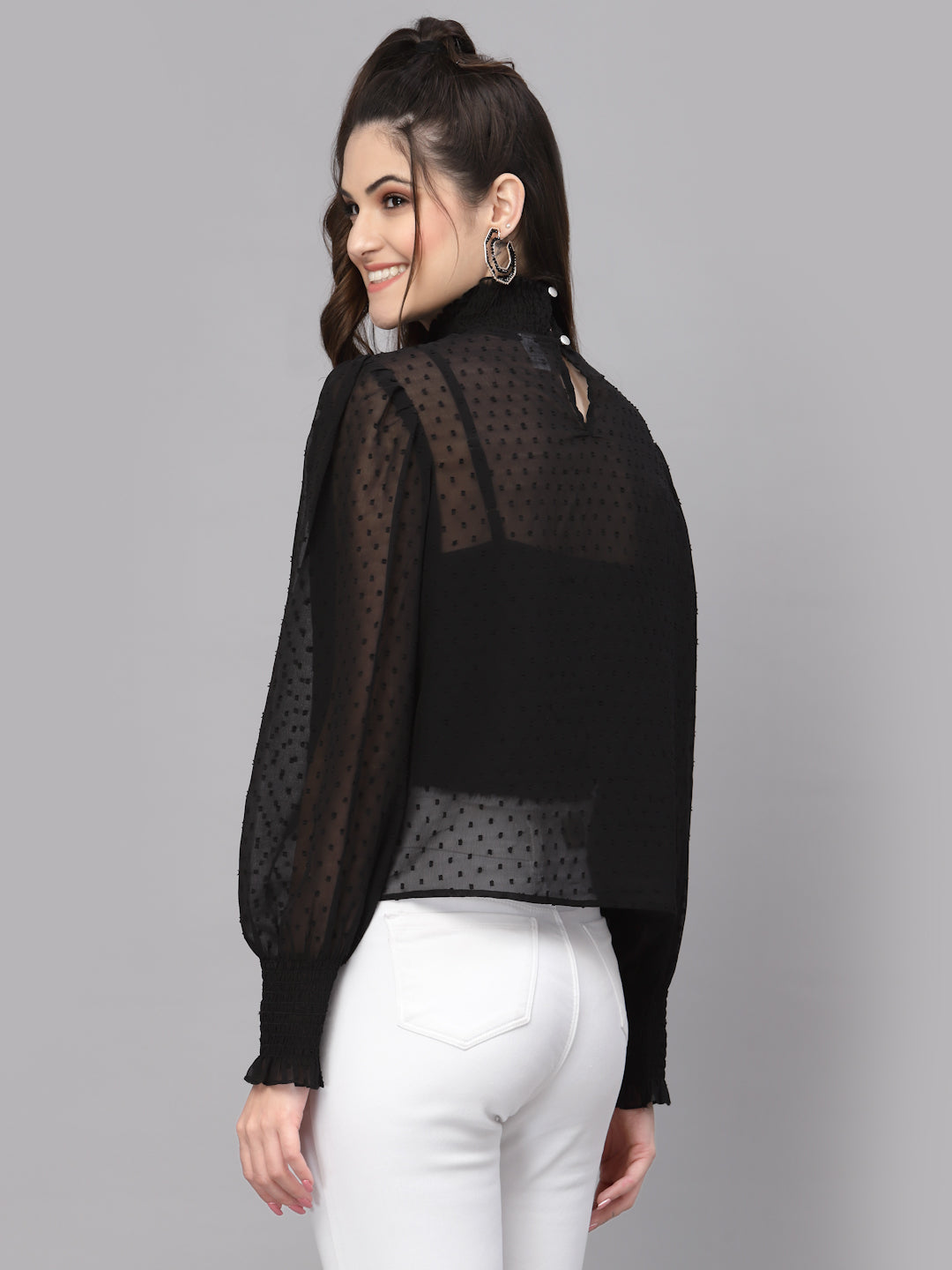 Woman wearing a black sheer top with white pants on a gray background