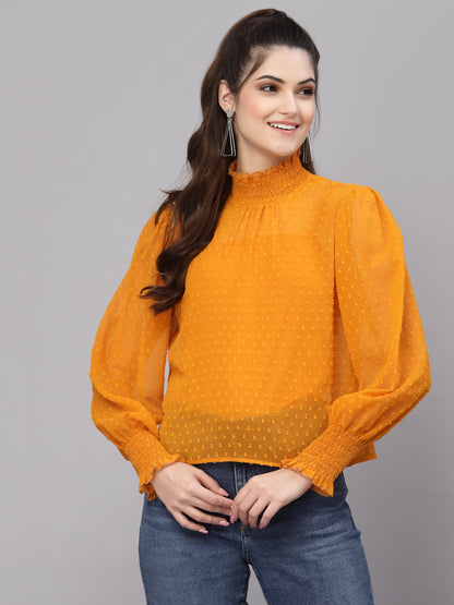 Woman wearing an mustard blouse with long sleeves and a high collar on a gray background