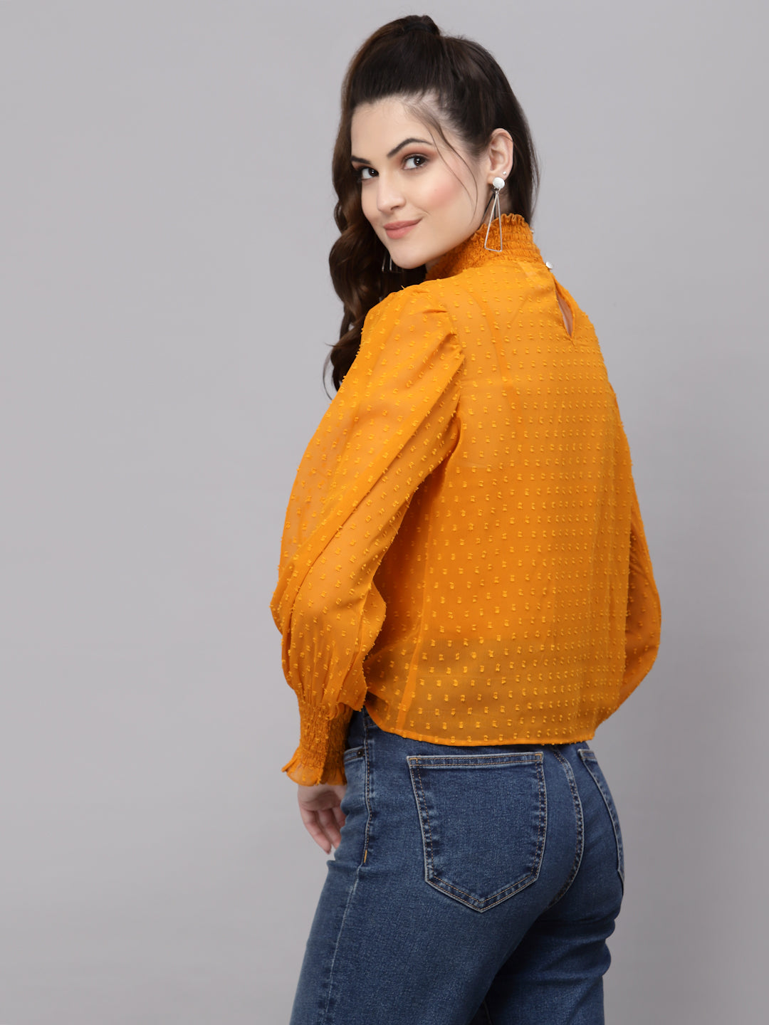Woman wearing an mustard top and blue jeans on a gray background