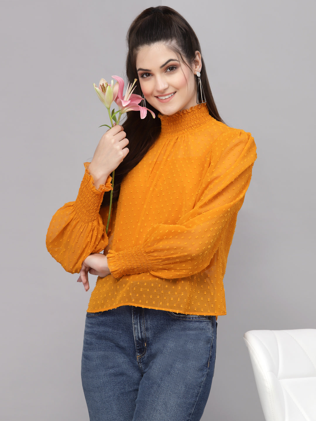 Woman wearing an mustard top holding flowers against a gray background