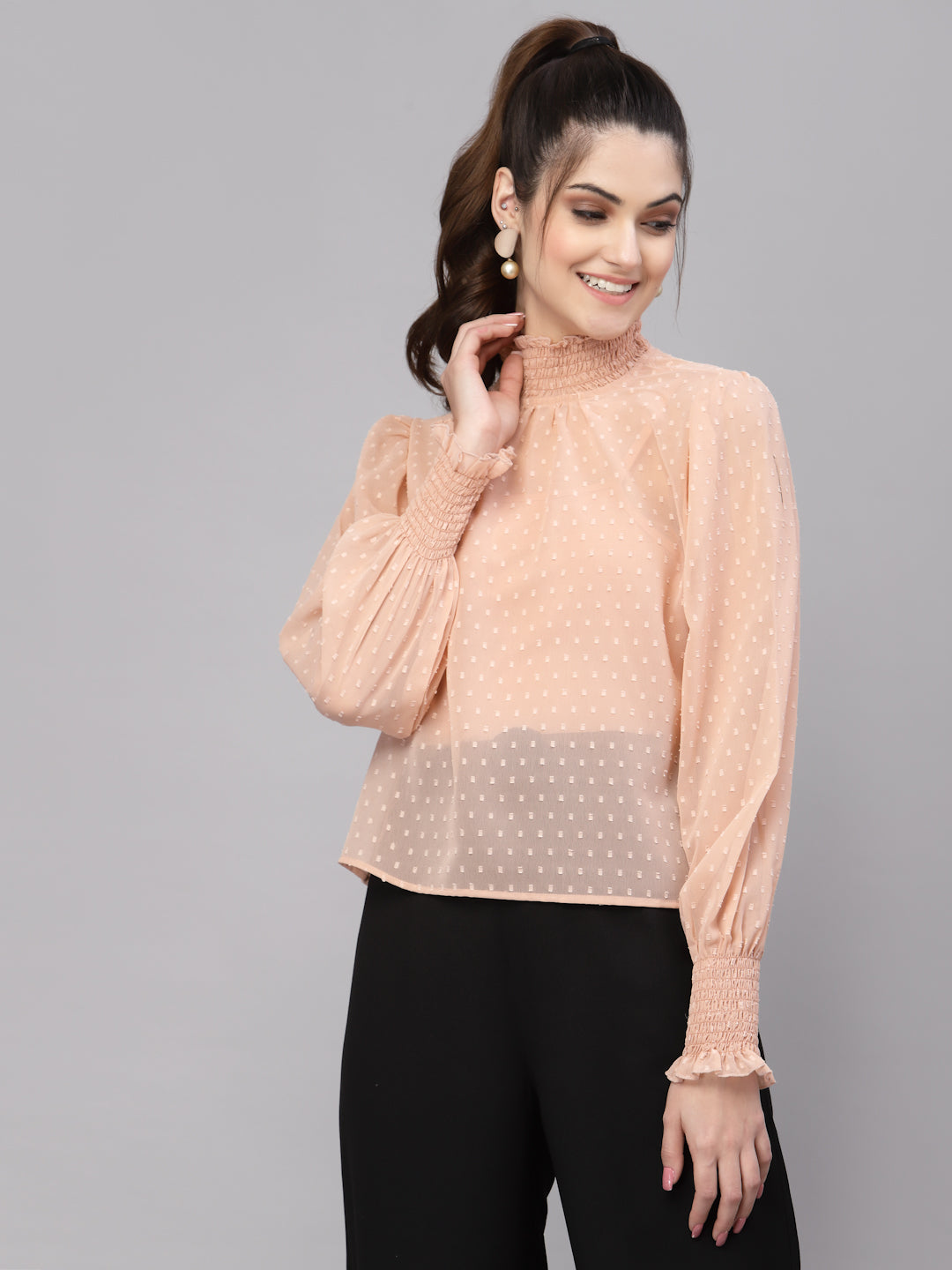 Woman wearing a peach top with sheer overlay on a gray background