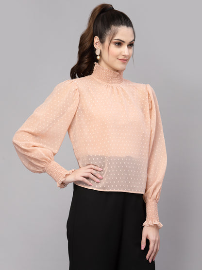 Woman wearing a peach blouse with long sleeves and black pants on a gray background