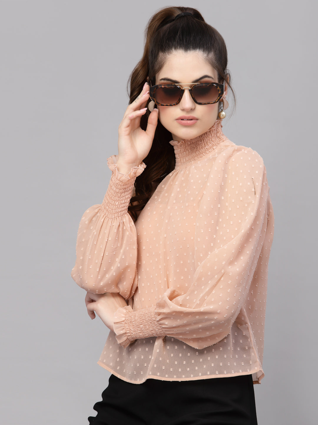 Woman wearing a light pink blouse with puffed sleeves and sunglasses on a gray background