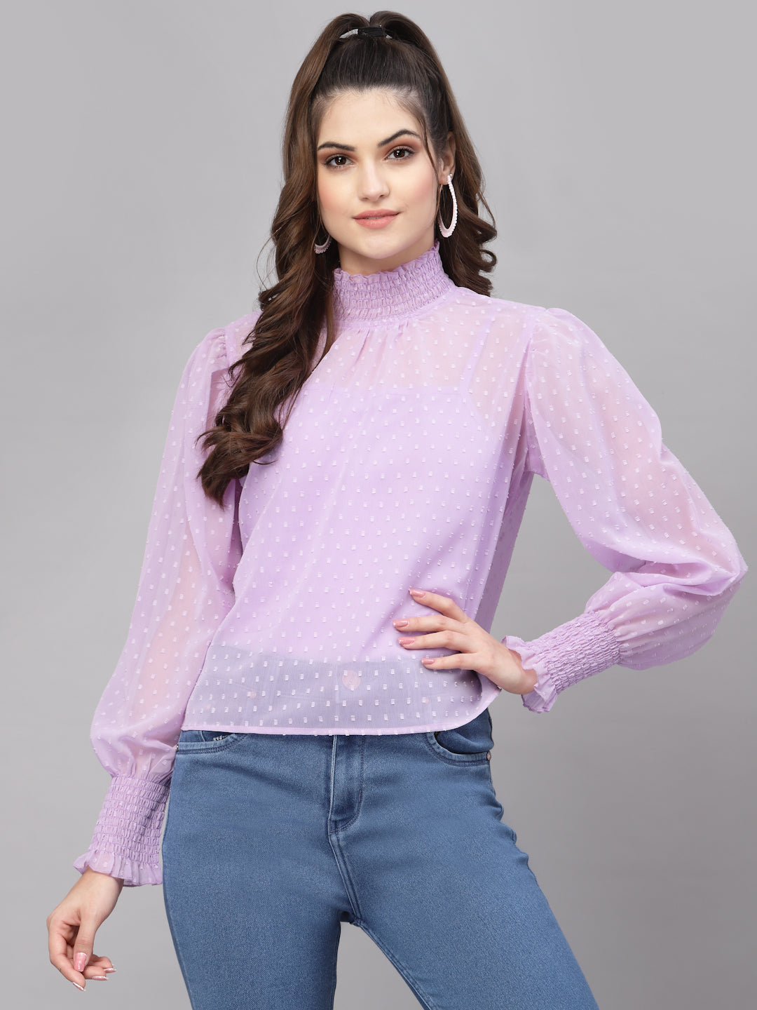 Woman wearing a purple top with long sleeves and blue jeans on a gray background