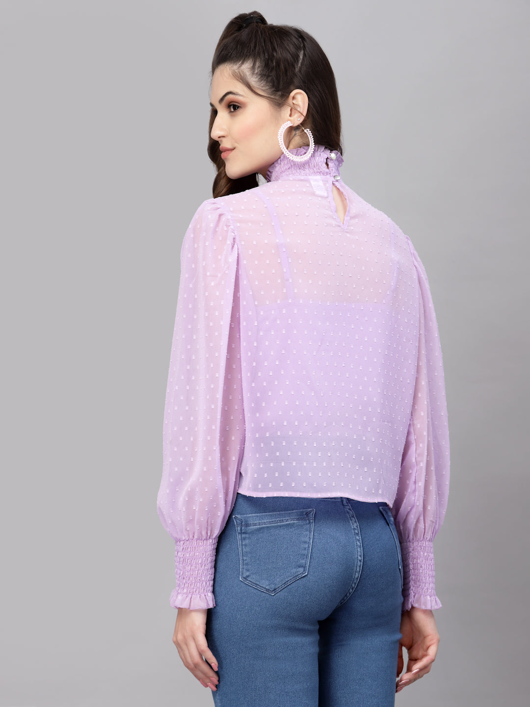 Woman wearing a light purple top with a subtle pattern and blue jeans on a gray background