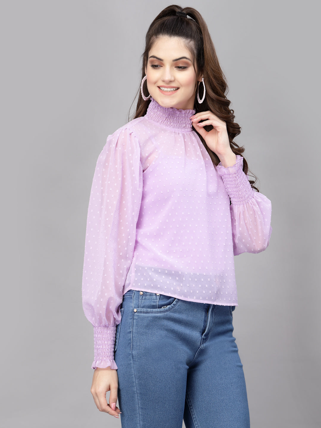 Woman wearing a purple top with sheer sleeves against a gray background