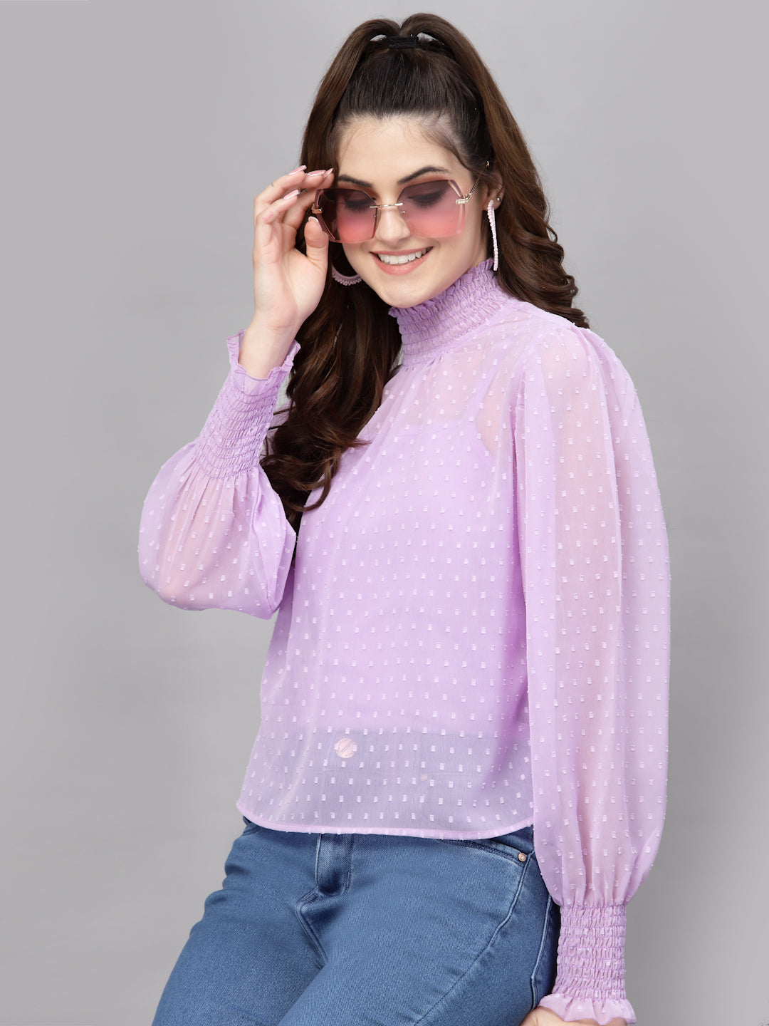 Woman wearing a light purple blouse with long sleeves and blue jeans on a gray background