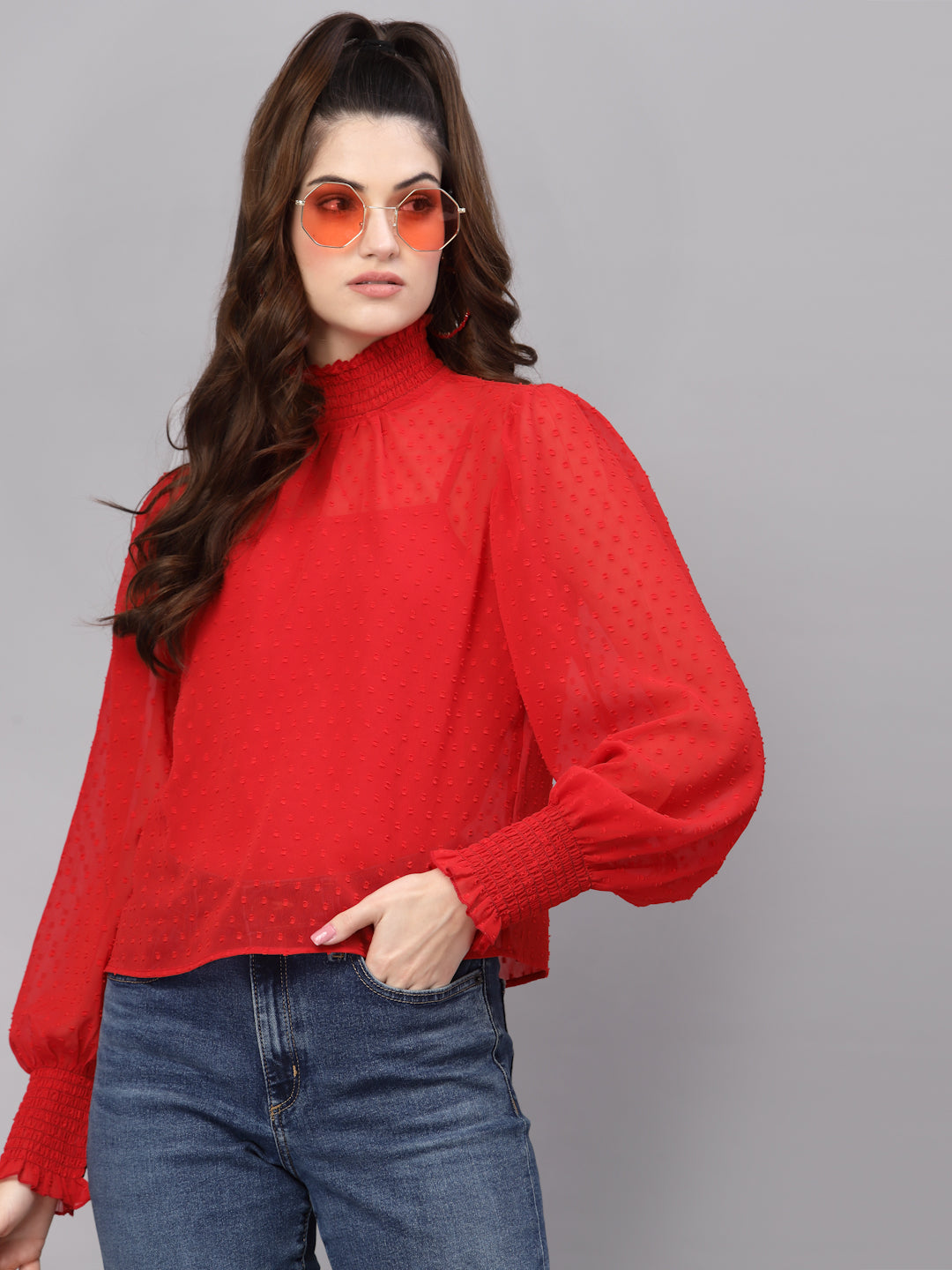 Woman wearing a red top and blue jeans against a gray background