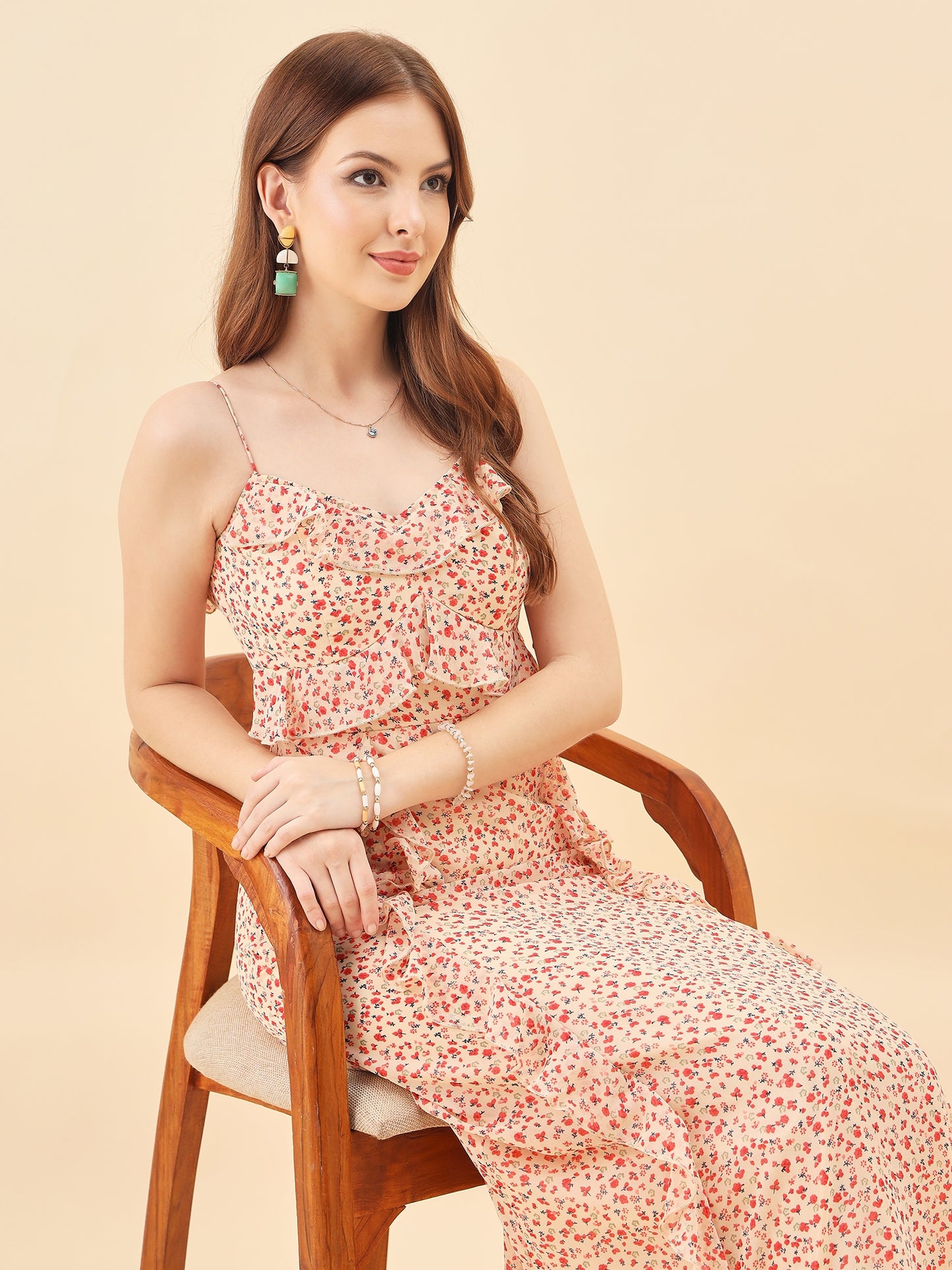 Woman in a floral dress sitting on a wooden chair against a beige background