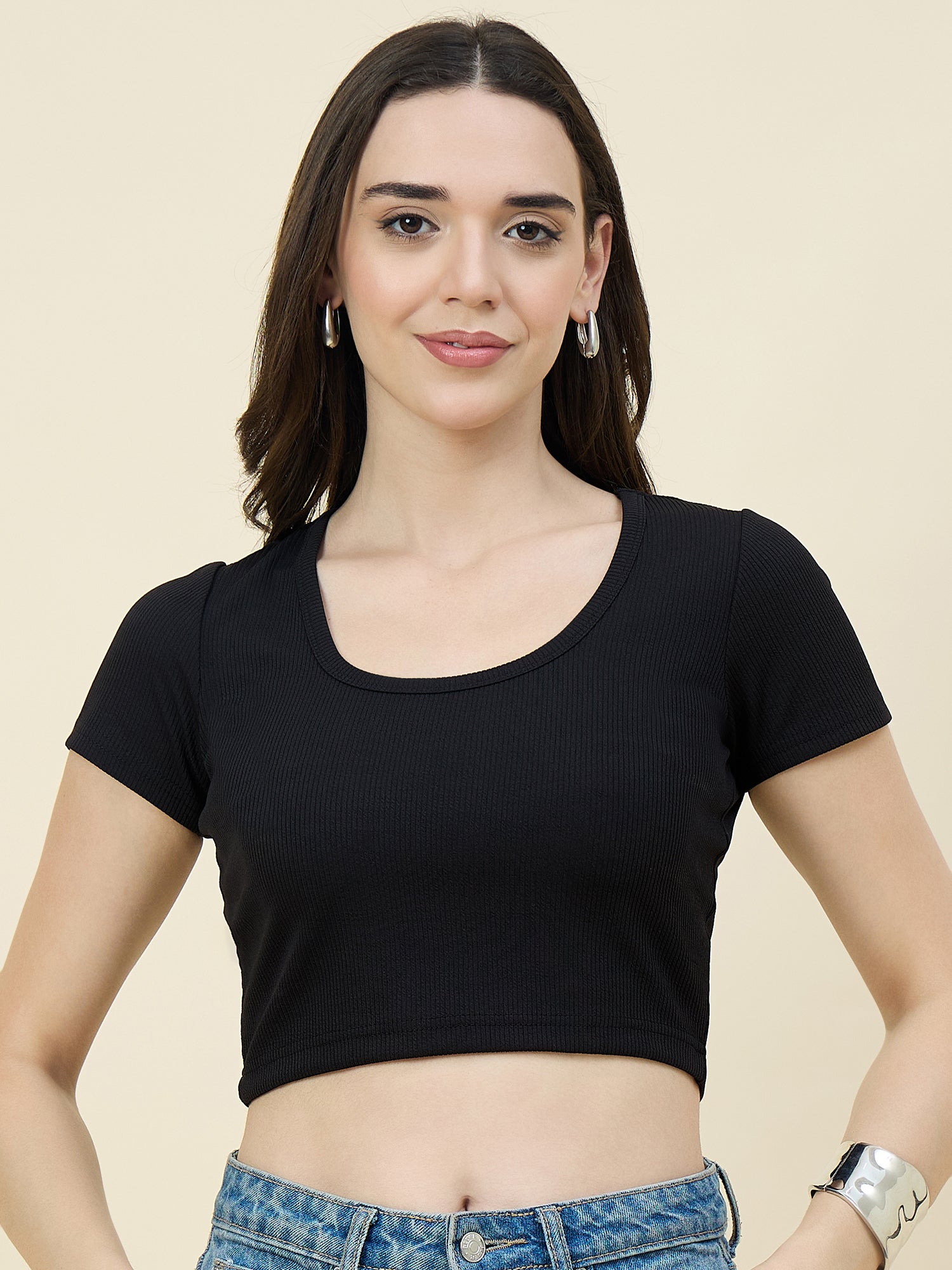 Woman wearing a black crop top and blue jeans against a beige background
