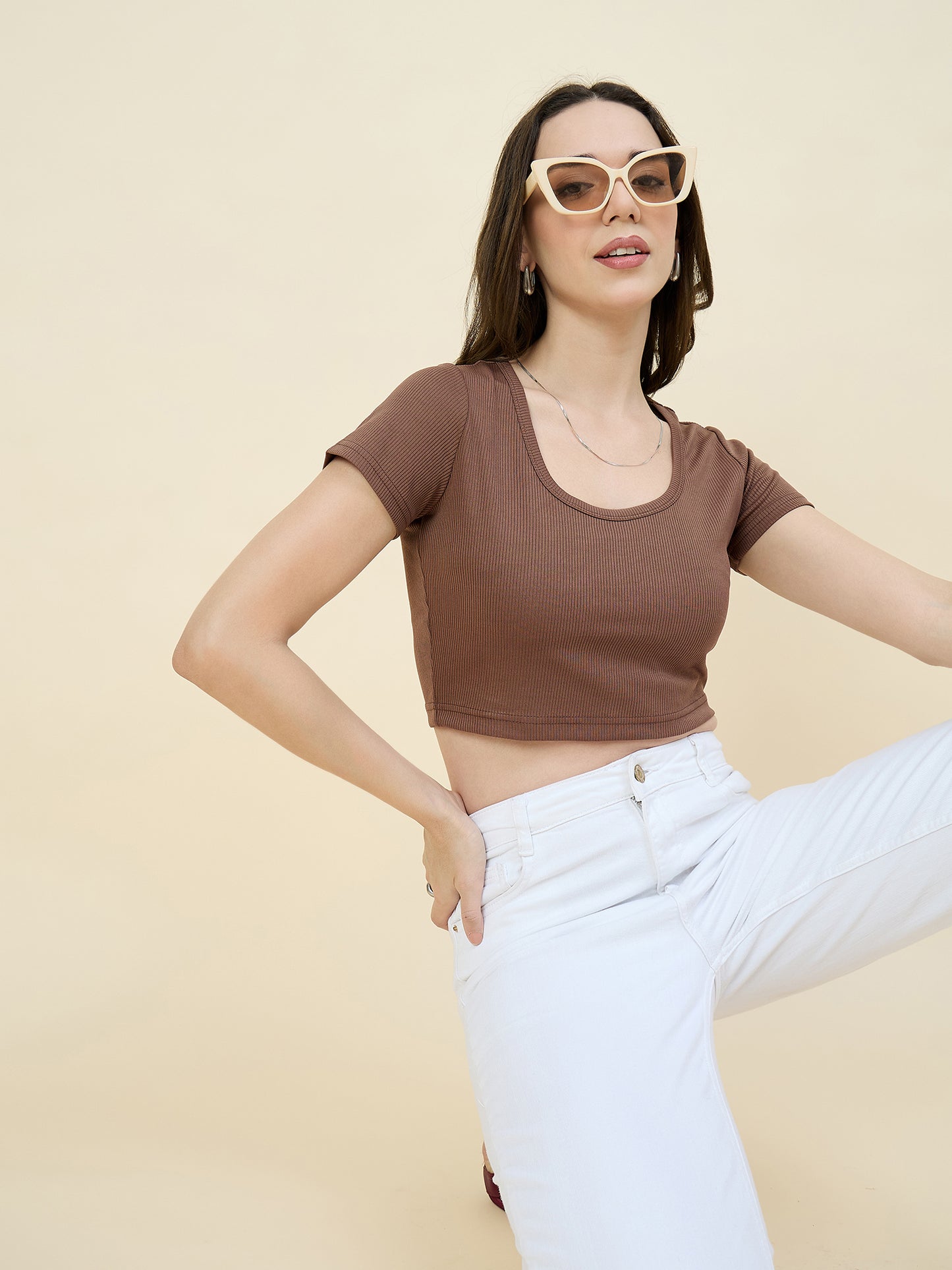 Woman wearing a brown crop top and white pants against a beige background