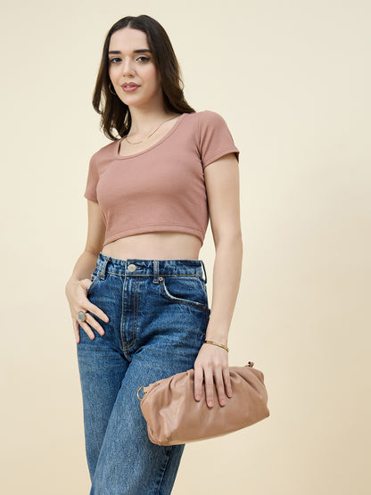 Woman wearing a cream crop top and blue jeans, holding a brown clutch against a beige background