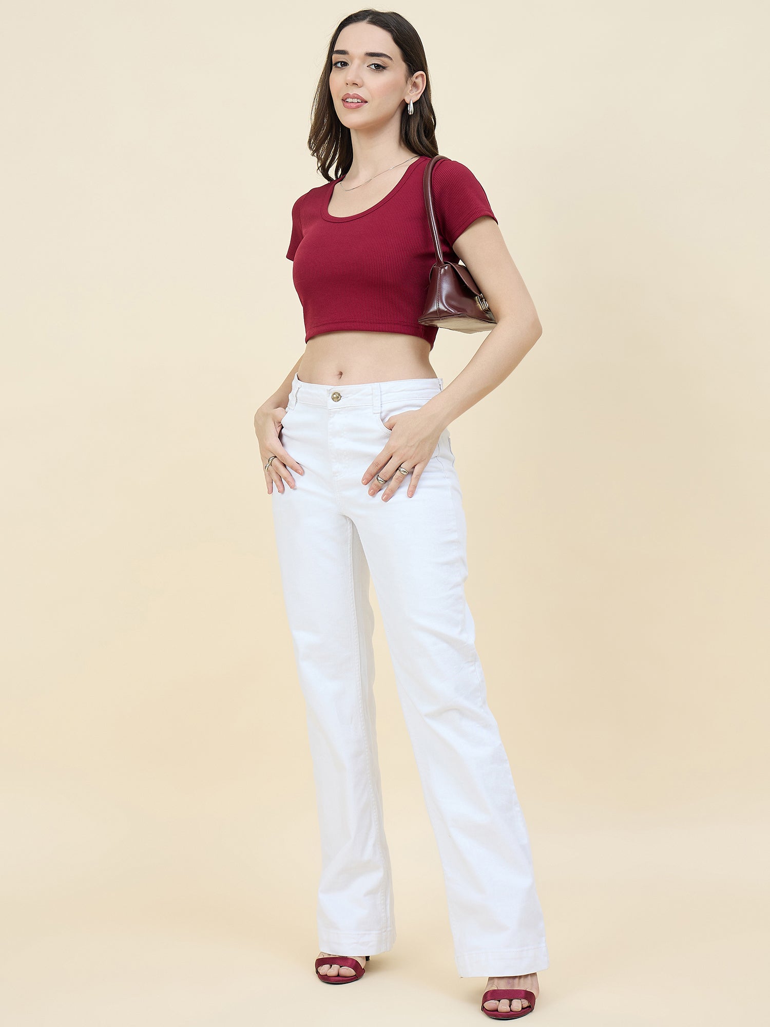 Woman wearing a maroon top and white jeans on a beige background