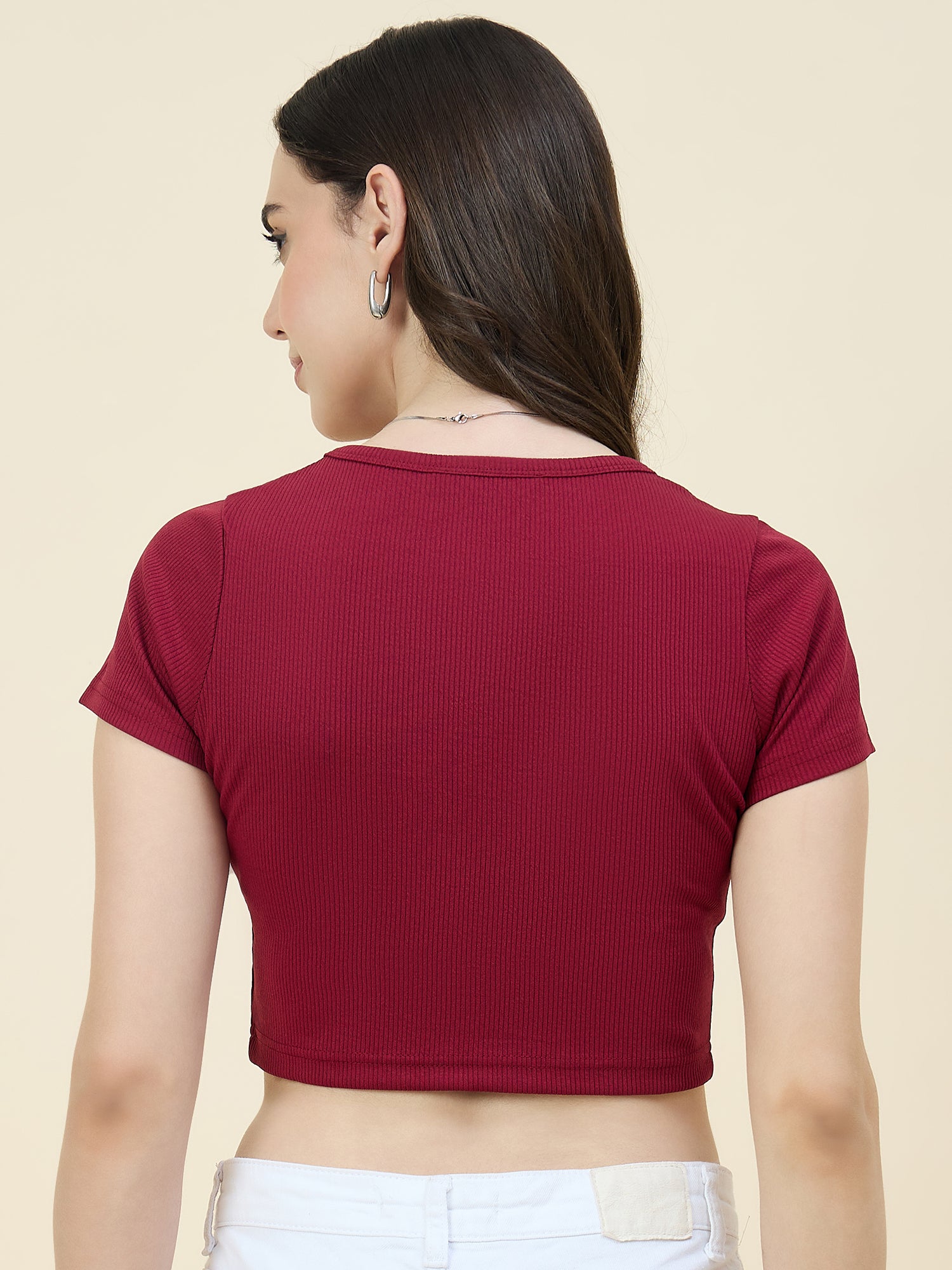 Woman wearing a maroon ribbed crop top on a beige background