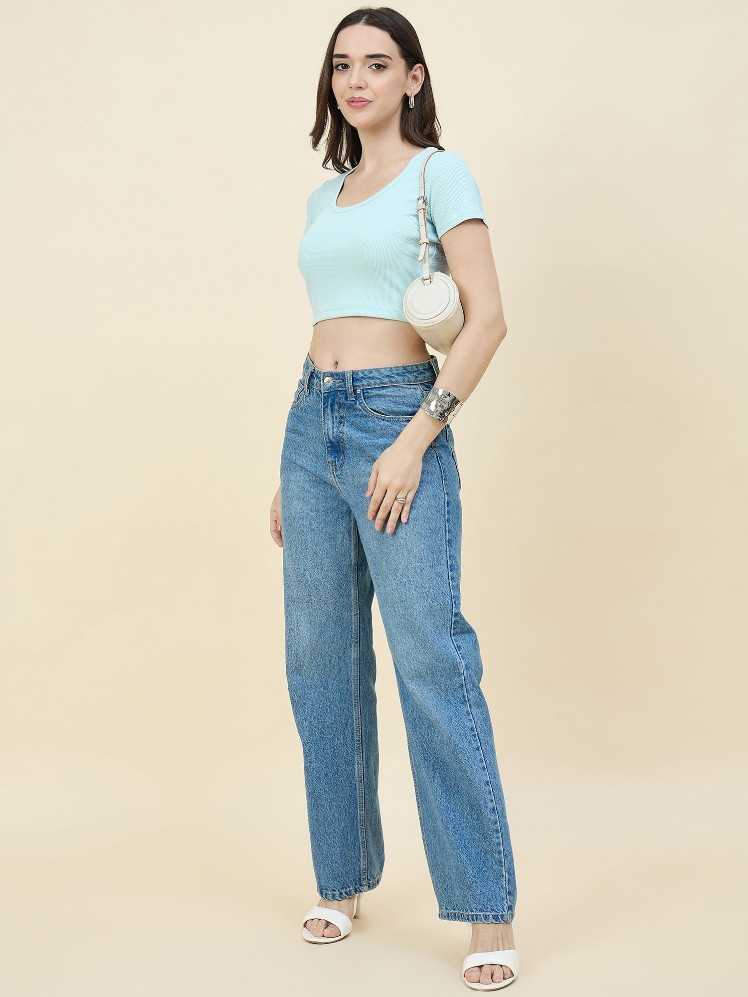 Woman wearing a Sky blue crop top and jeans on a beige background
