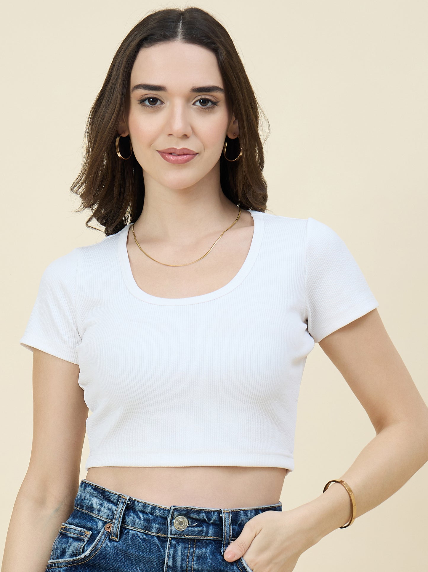 Woman wearing a white crop top and blue jeans against a beige background