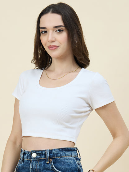 Woman wearing a white crop top and blue jeans against a beige background