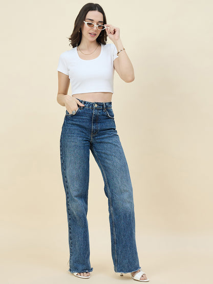 Woman wearing a white crop top and blue jeans against a beige background