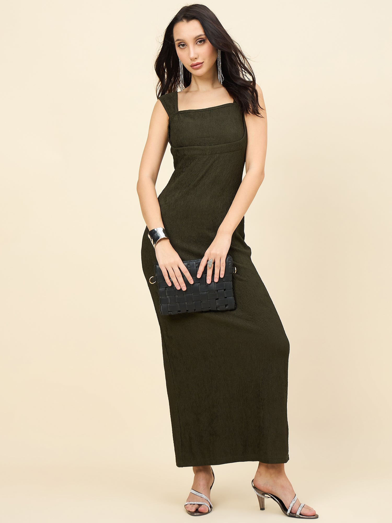 Woman wearing a green dress holding a black clutch against a beige background