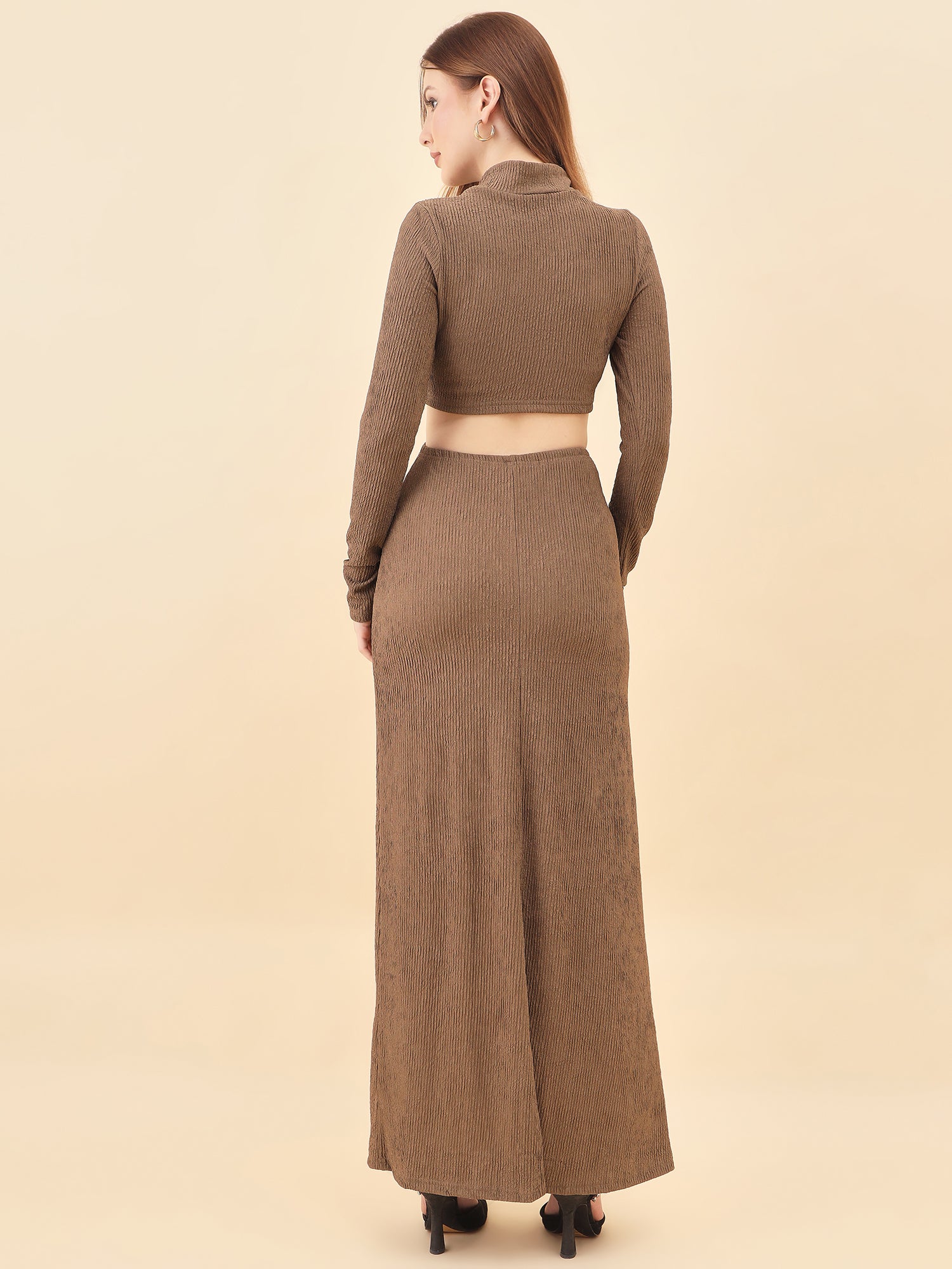 Woman wearing a brown two-piece outfit with a long skirt and cropped top on a beige background
