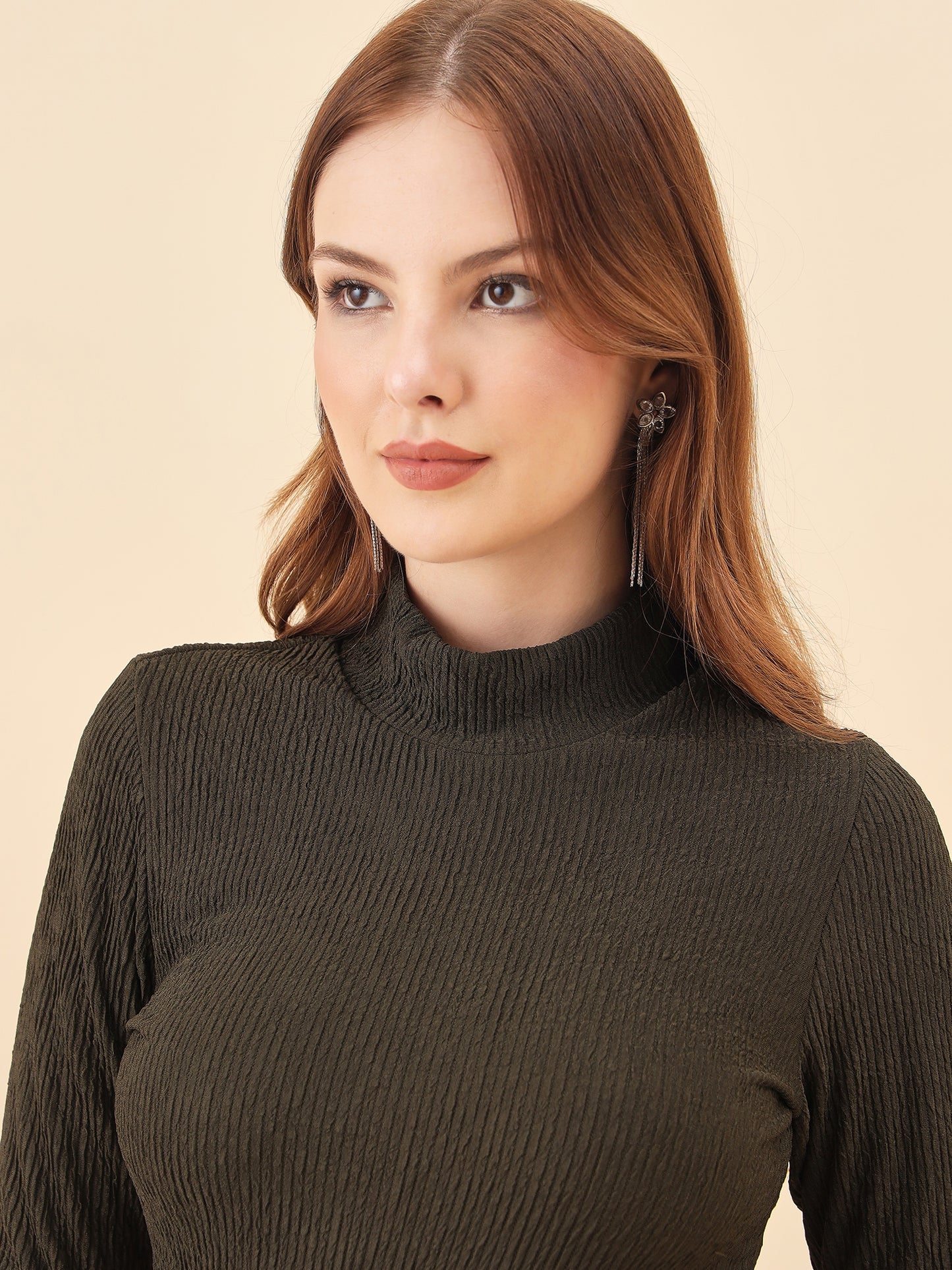 Woman wearing a dark ribbed sweater against a beige background