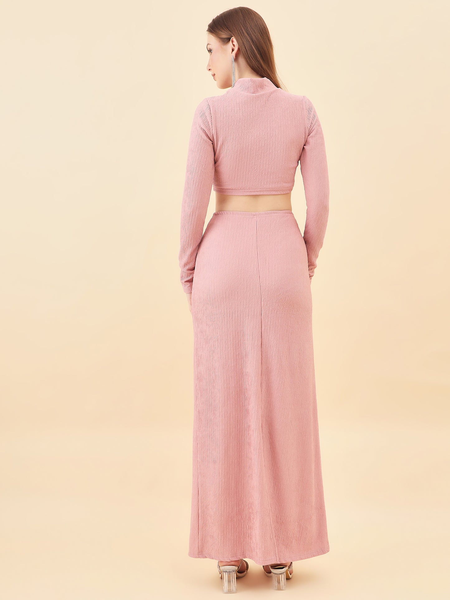 Woman wearing a pink outfit with a long dress and jacket on a beige background