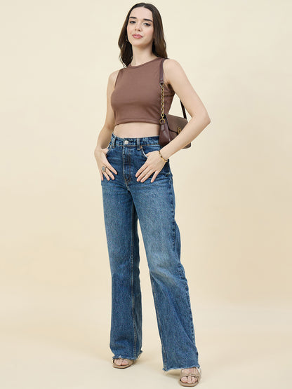 Woman wearing a brown sleeveless top and blue jeans on a beige background