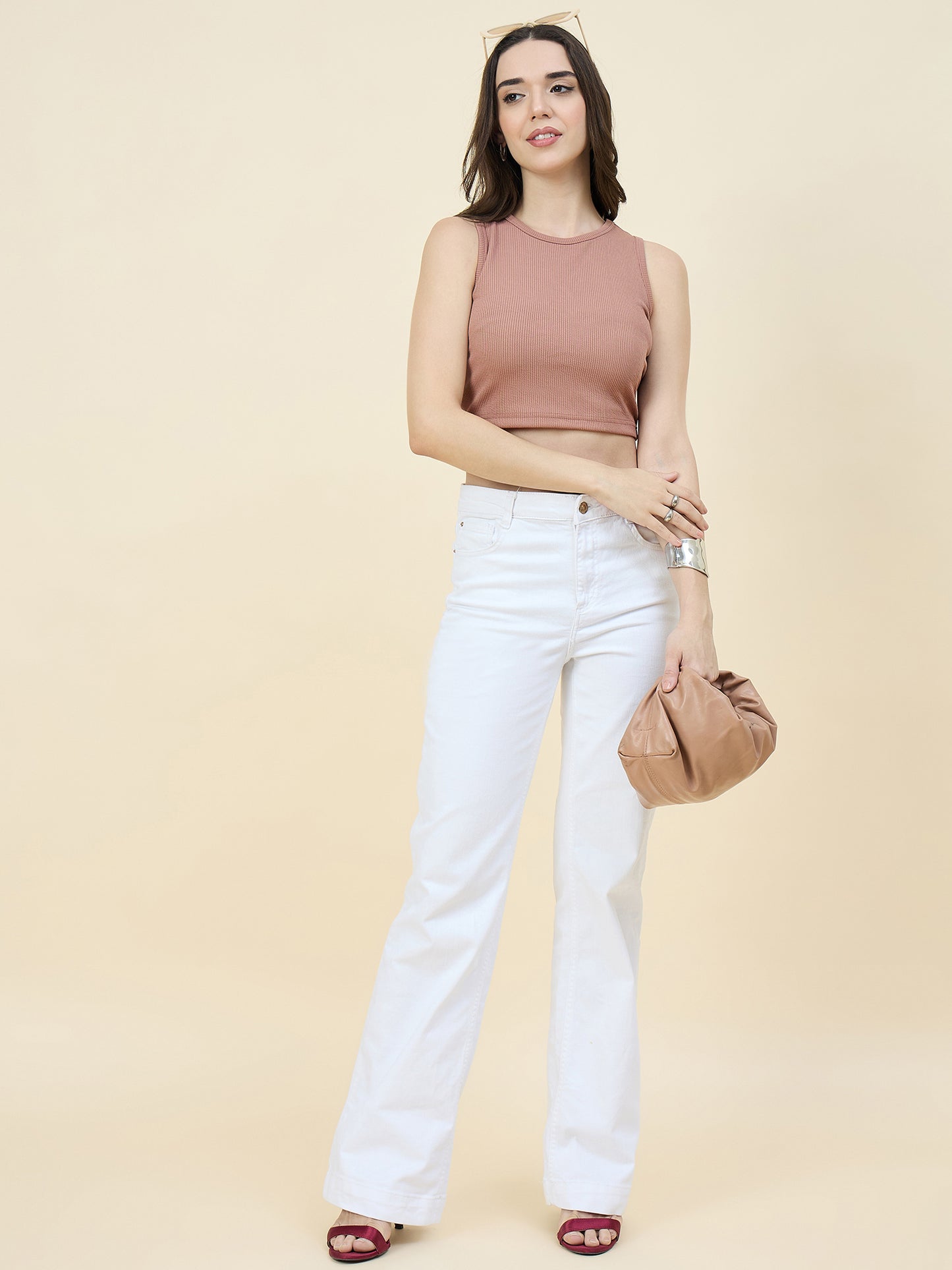 Woman wearing a cream top and white pants holding a beige handbag on a beige background