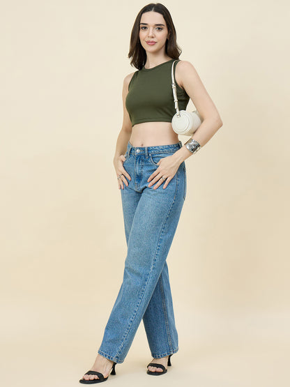 Woman wearing a green crop top and blue jeans against a beige background