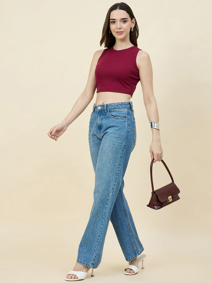 Woman wearing a maroon sleeveless top and blue jeans, holding a brown handbag on a beige background