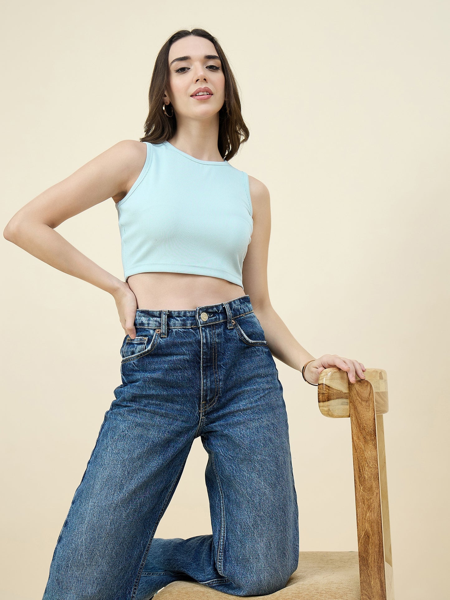 Woman wearing a Sky blue tank top and blue jeans against a beige background