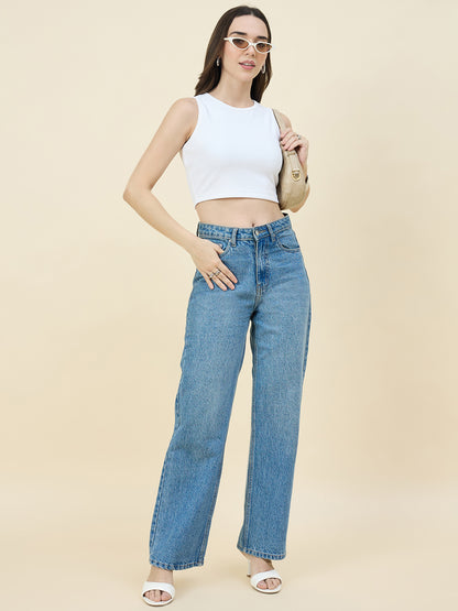 Woman wearing a white crop top and blue jeans on a beige background