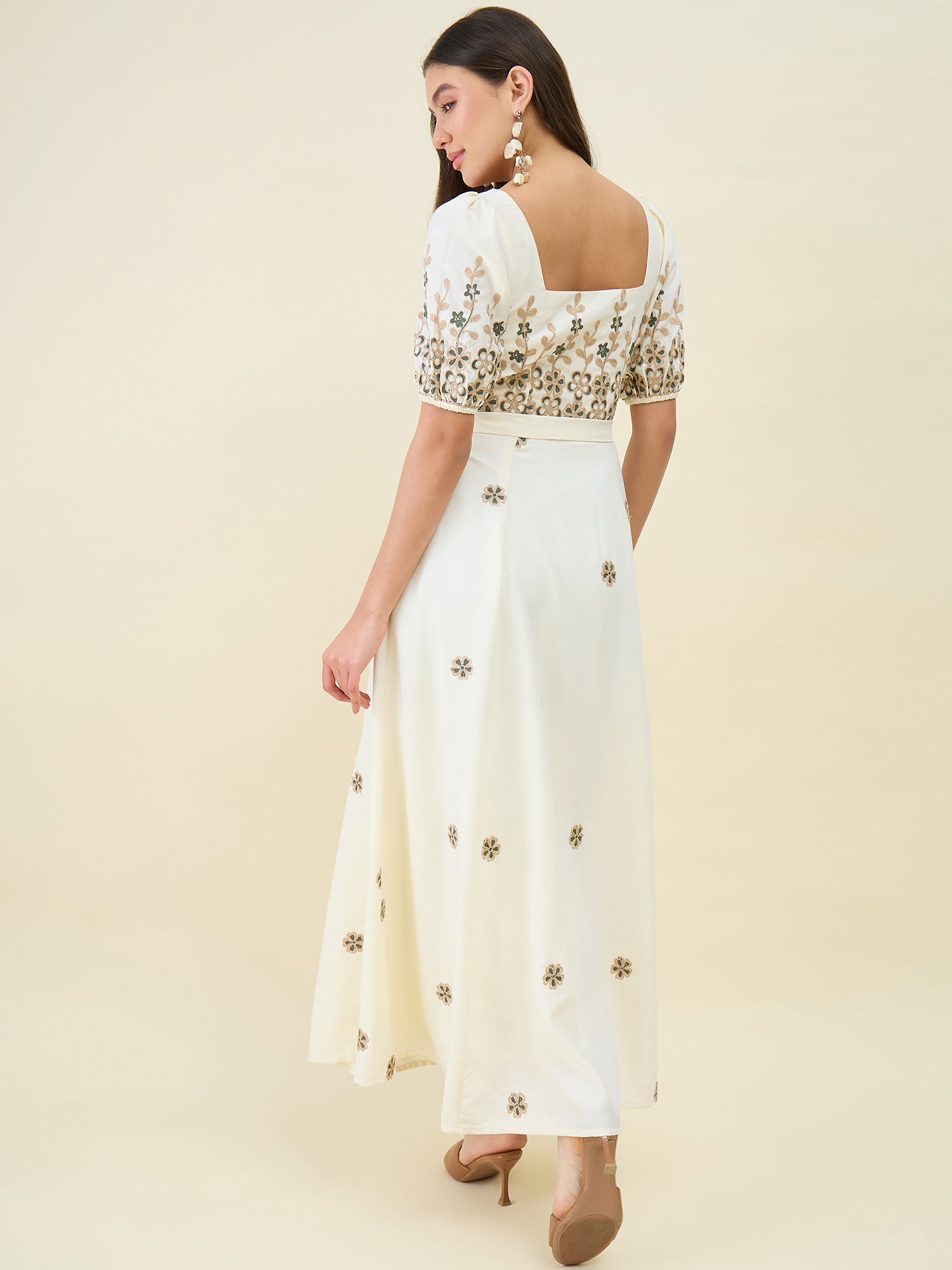 Woman wearing a white outfit with gold floral patterns on a beige background