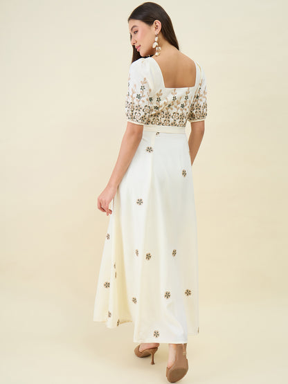 Woman wearing a white outfit with gold floral patterns on a beige background