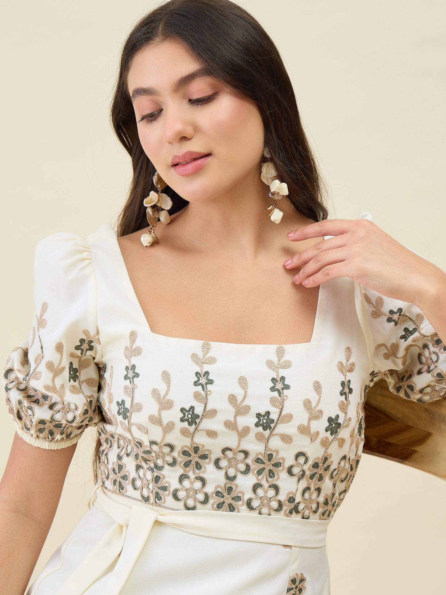 Woman wearing a white blouse with floral embroidery on a beige background