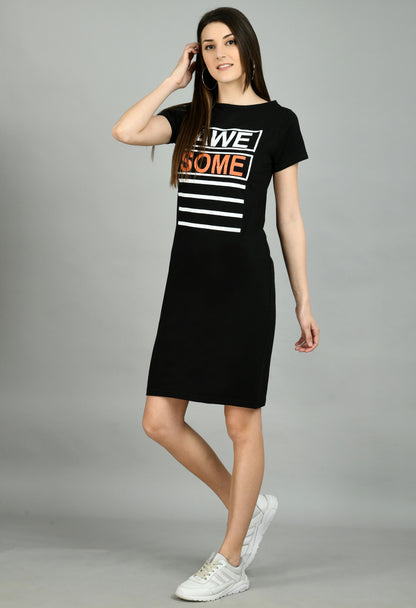 A woman standing in a studio setting, wearing a black t-shirt dress with text graphics, paired with white sneakers.