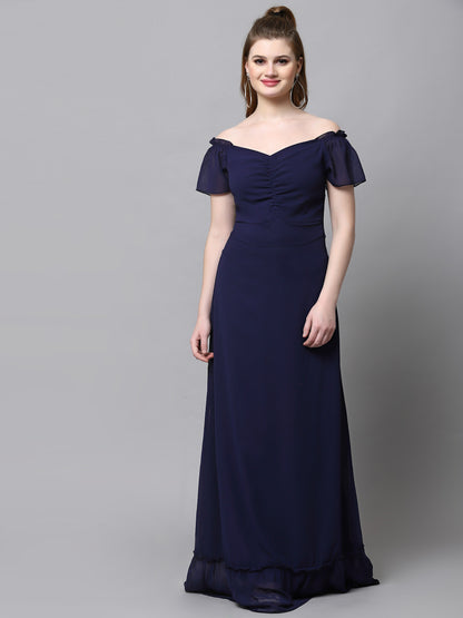 A woman standing, wearing a blue maxi dress with short flutter sleeves and a V-neckline.