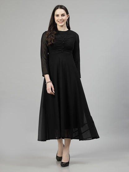 A woman standing and smiling, wearing a black long-sleeved fit and flare dress with lace detailing.