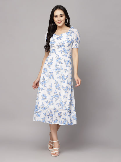 A woman wearing a white and blue floral print A-line dress with short sleeves and a flared hemline.